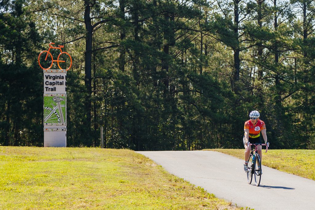 Cyclists on the trail at Dorey Park with the Virginia Capital Trail marker in the background.