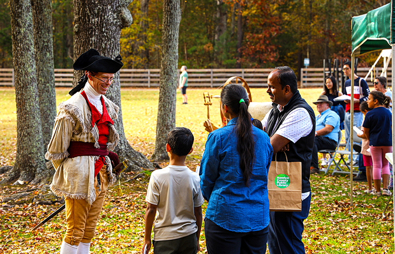 A Revolutionary War reenactor visits with several adults and children.