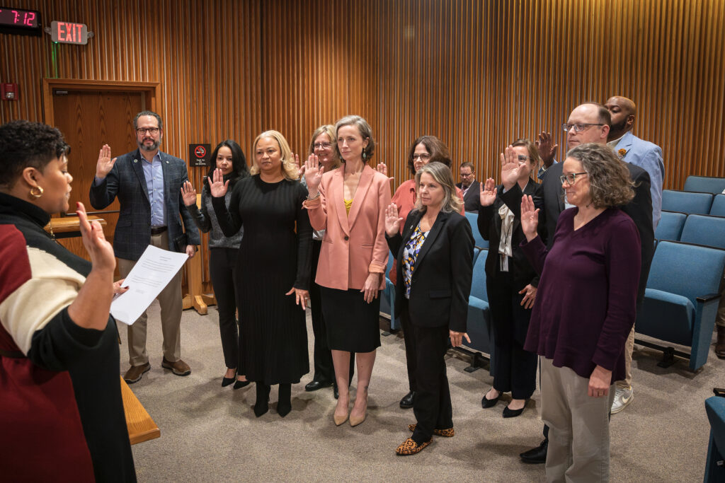 Eleven people stand and raise their right hand to get sworn in to the SRAC Committee while another person reads off of a script.