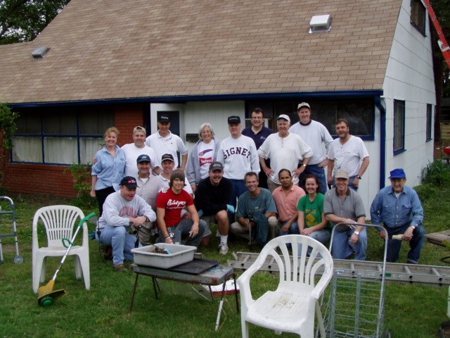 Photo of a group of people posing outside ofa home with lawn equipment and ladders.