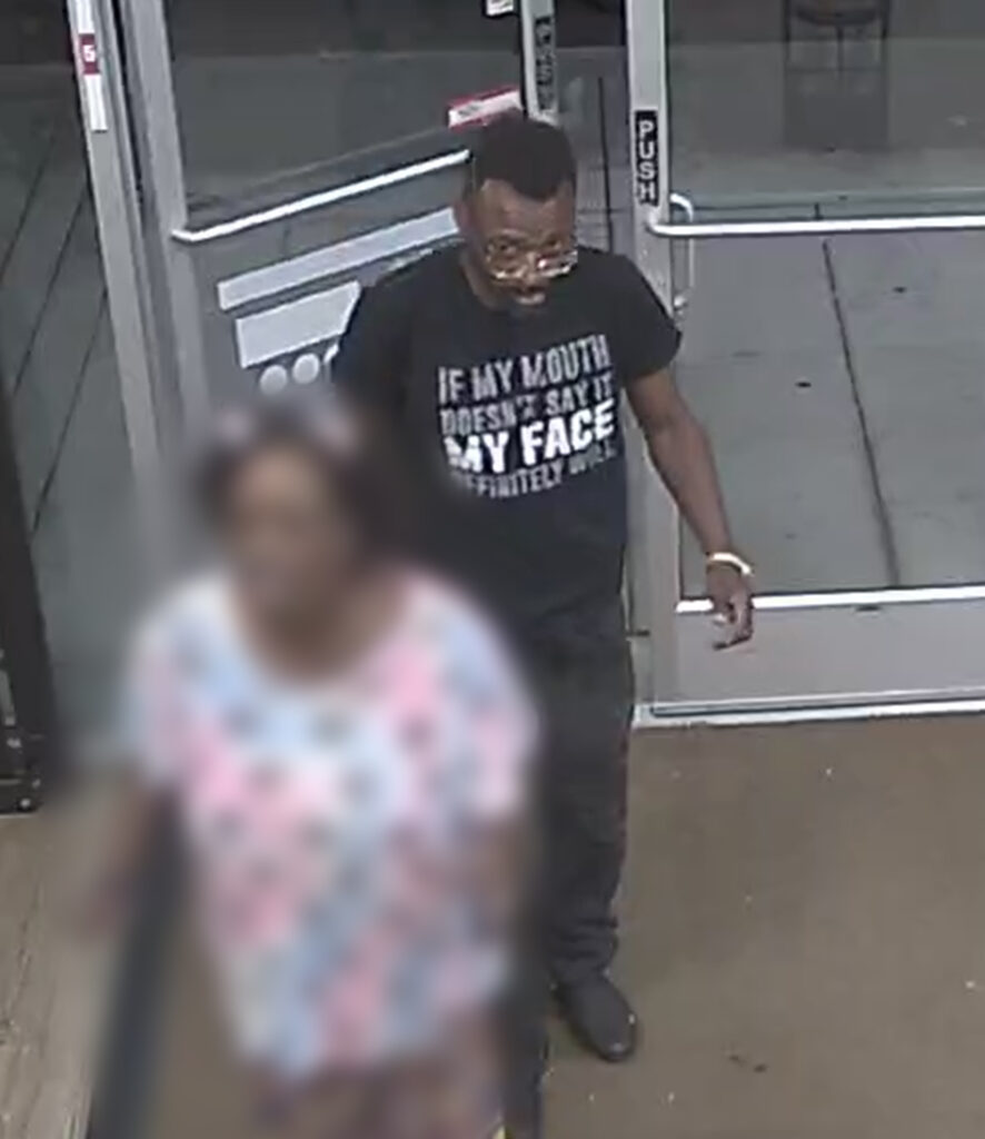 Image shows a Black male in a black shirt with glasses entering a business.
