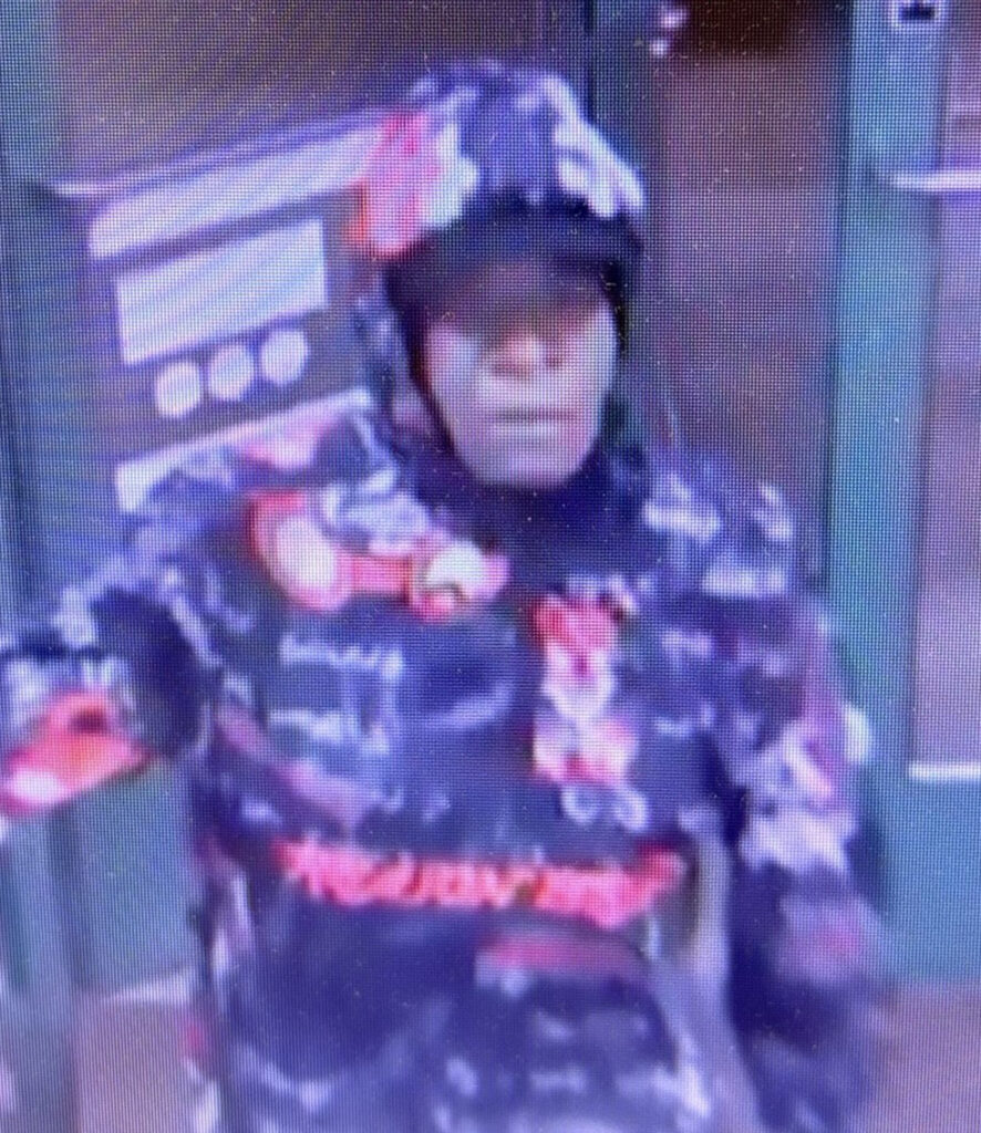 Image shows a Black male, wearing a red, black and white colorful jacket with the hood on entering a store.