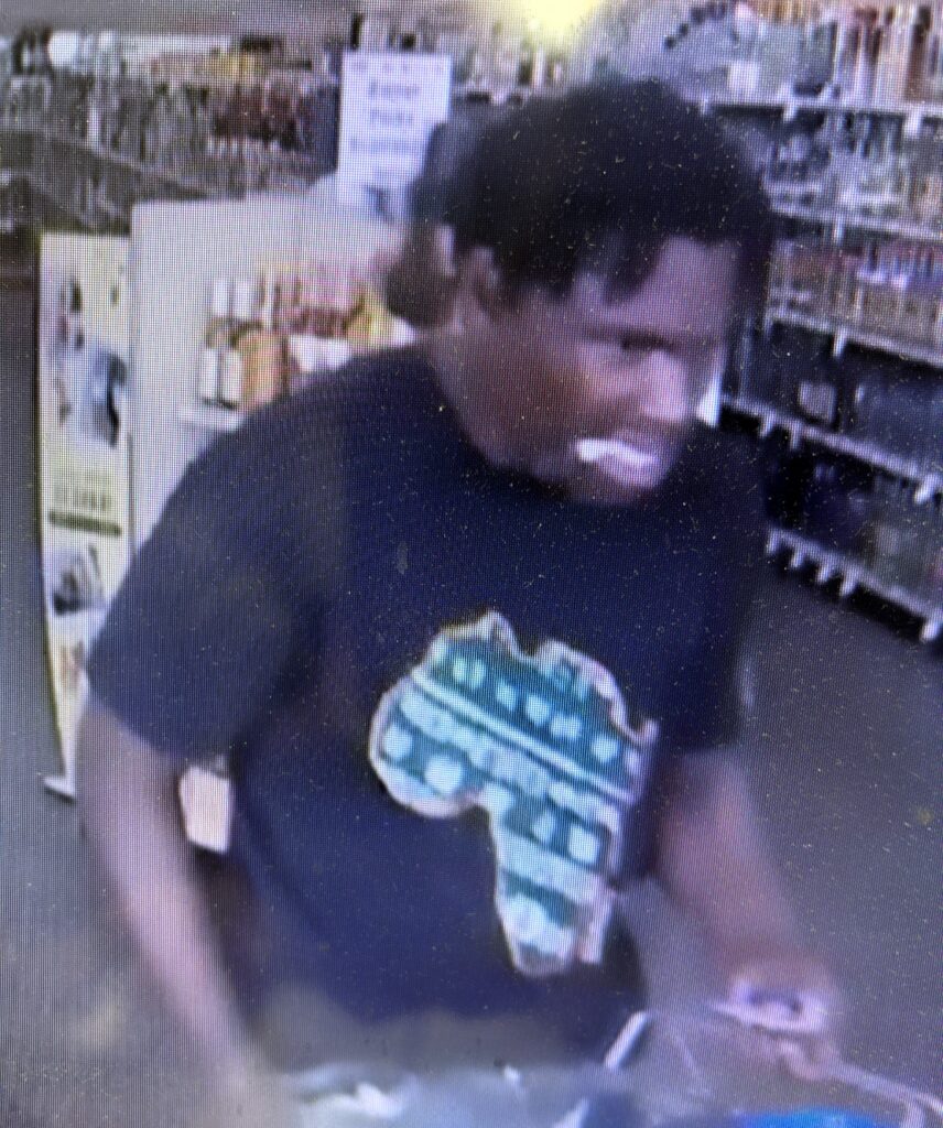Surveillance screenshot of a person inside an ABC store. They're wearing a dark shirt with the shape of Africa on it.