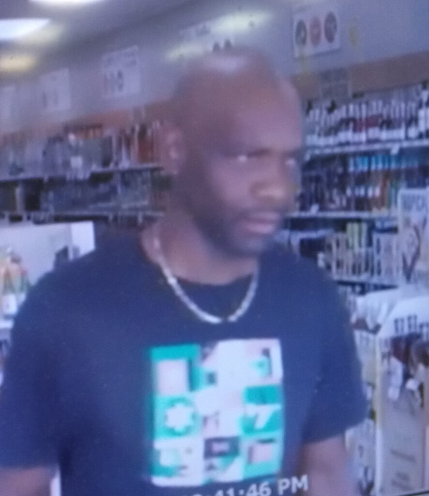 Surveillance screenshot of a person inside an ABC store. They're wearing a dark shirt and necklace.