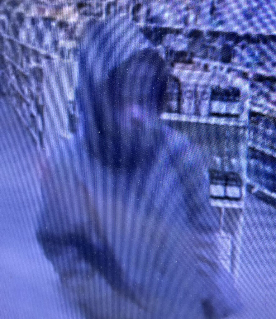 Person wearing a hooded jacket walking through a store aisle filled with various products on shelves.
