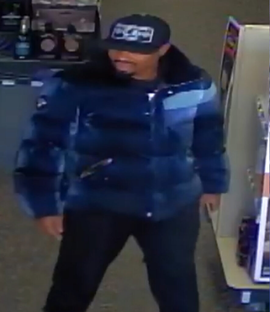 Person wearing a dark blue puffer jacket and black pants standing near store shelves with blurred face.