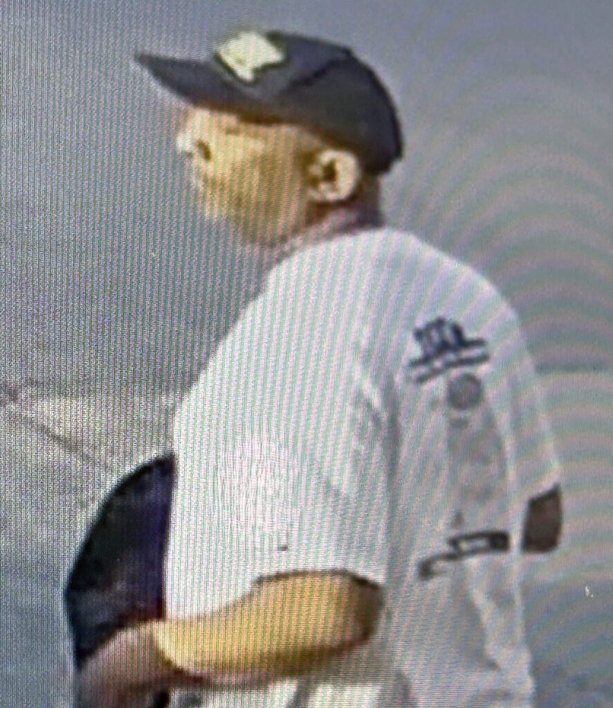 A snapshot of a man wearing a baseball hat walking in a parking lot.