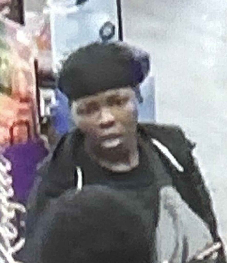 A person wearing a dark colored hat and clothing in an ABC Store.