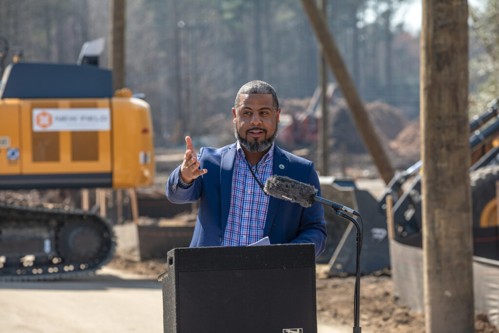 Public Works Director Terrell Hughes speaks at a lectern in front of construction equipment.