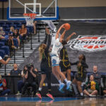 A women's college basketball player attempts a shot near the basket while contested by two opposing players.