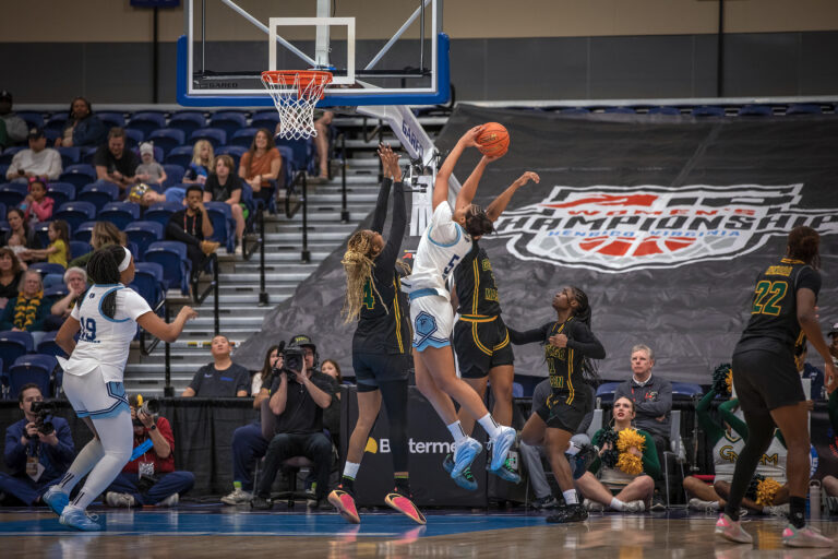 A women's college basketball player attempts a shot near the basket while contested by two opposing players.