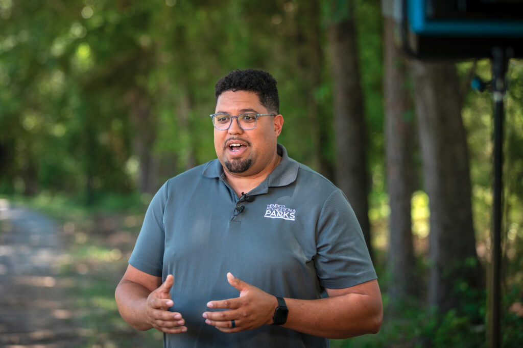 An official speaks to a reporter with woods in the background.