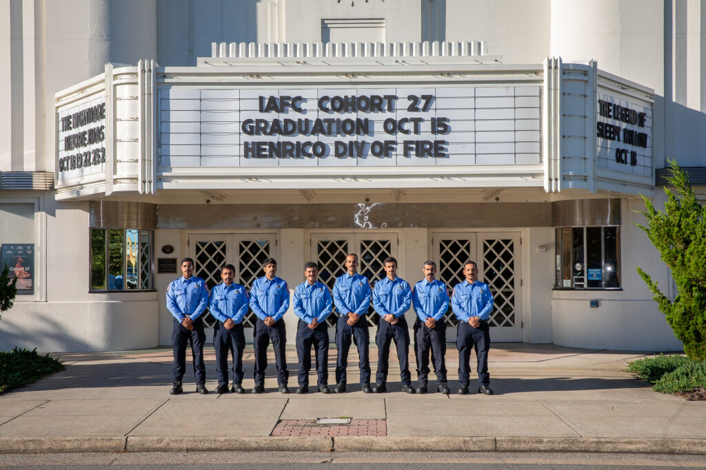 Eight Saudi firefighters pose outside Henrico Theatre. Marquee reads, IAFC Cohort 27 graduation Oct. 15 Henrico Div of Fire.