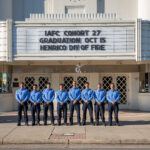 Eight Saudi firefighters pose outside Henrico Theatre. Marquee reads, IAFC Cohort 27 graduation Oct. 15 Henrico Div of Fire.