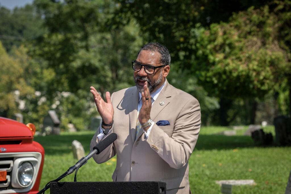 A speaker at a lectern applauds.