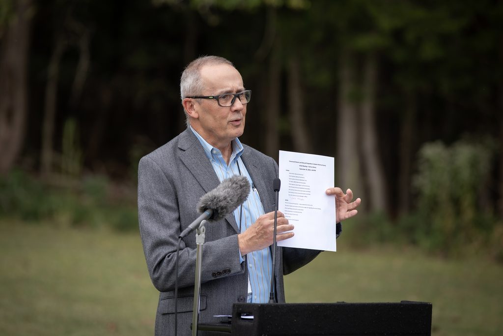 Deputy County Manager Steve Yob holds up a piece of paper at the lectern.