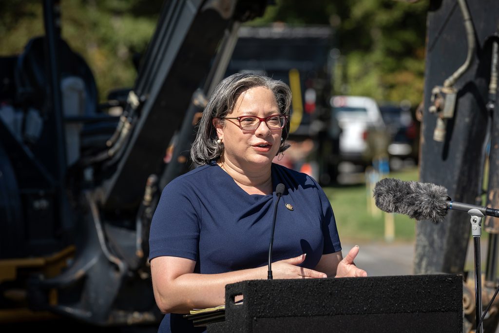 U.S. Rep. Jennifer McClellan speaks at a lectern with a bulldozer in the background.