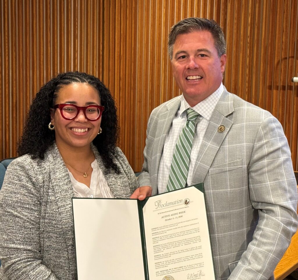 Two individuals pose for a photo holding a proclamation for active aging week.