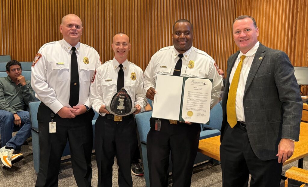 Three fire officials and an elected official pose with one hold a proclamation for fire prevention week.