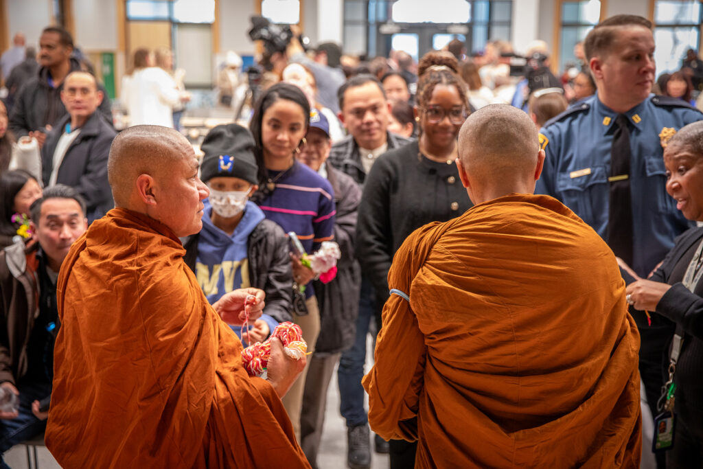 Two monks give out braided bracelets to a crowd of people.