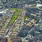 Aerial rendering of a large urban development plan featuring numerous buildings and green spaces nestled within a wooded area. The project is surrounded by roads and existing developments, with a prominent arena visible nearby.
