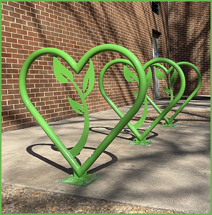 A row of three bright green, heart shaped bike racks next to a brick wall.