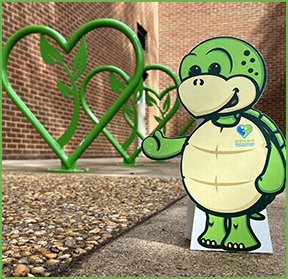 A cutout of Stewart the turtle gives a thumbs up to a row of green, heart shaped bike racks.