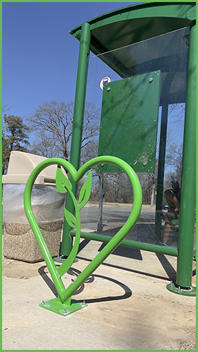 Photo of a bright green, HEART bike rack next to a bus stop.