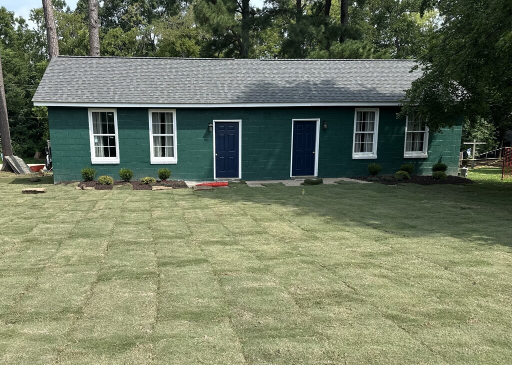 A green cabin has been built on a grassy lawn.