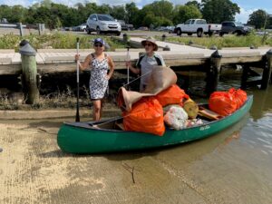 A man and woman standing next to a canoe full of orange litter bags.