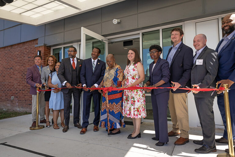 11 people holding a red ribbon with scissors in hand at Cool Lane Press Conference