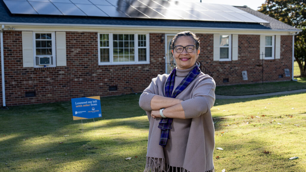 A photo of a woman standing in front of a house with solar panels on the roof.