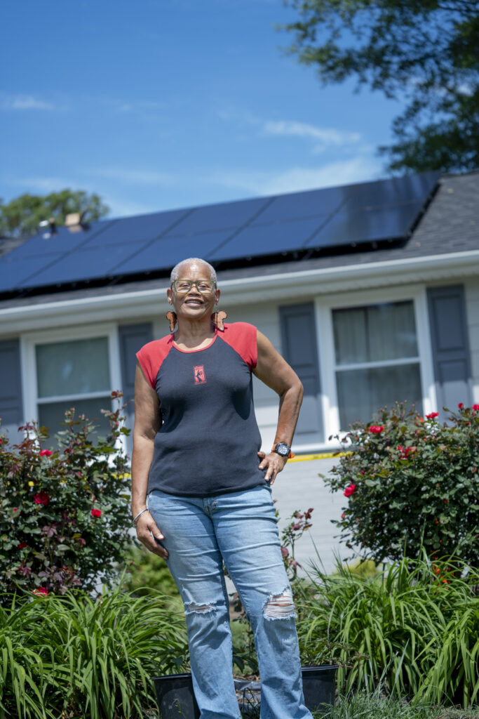 A photo of a woman standing in front of a house with solar panels on the roof.