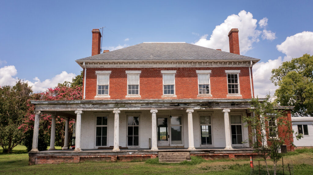 A historic home with a large, well-worn porch and matching chimneys.