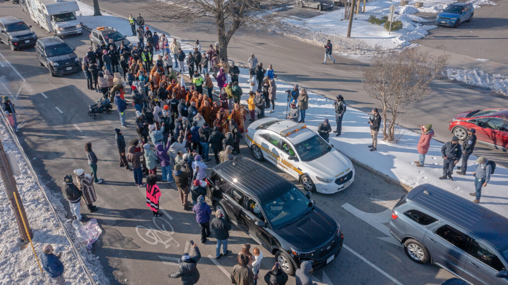 An aerial photo of monks on the Walk for Peace and hordes of supporters gathered along a snowy road.