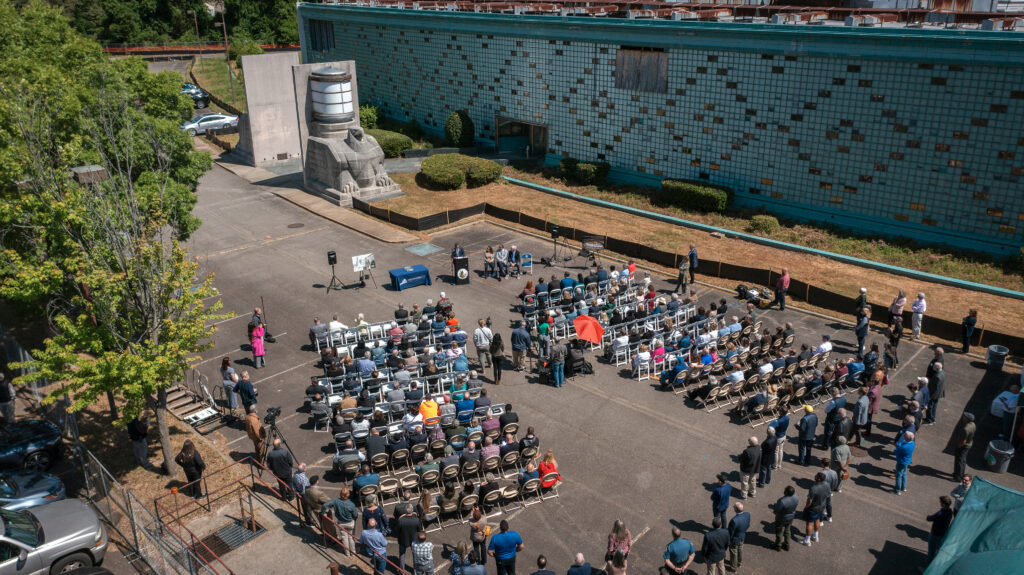 Arial photo of a news conference in a parking lot beside a building with a green glass facade.
