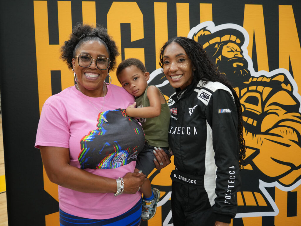 A Black woman in a NASCAR jumpsuit poses with her former teacher.