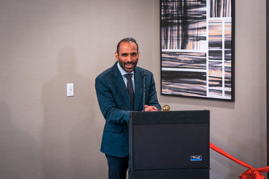 A man in a suit speaks at a lectern before a ribbon-cutting ceremony