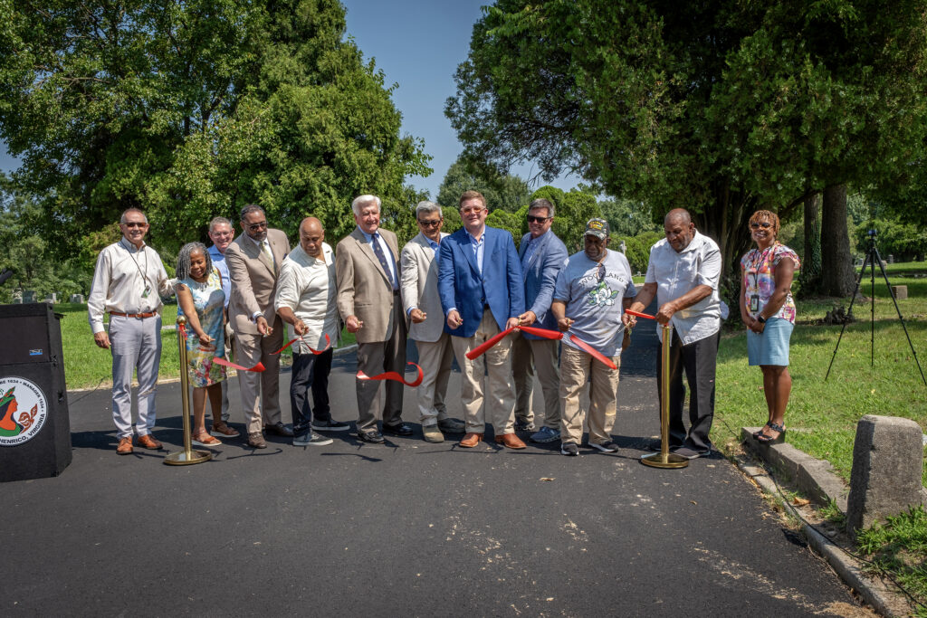 Officials stand for a ribbon-cutting at a cemetery celebrating newly paved roads.