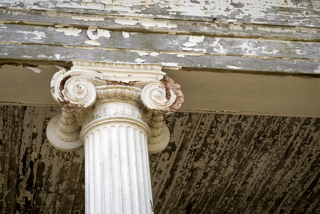 A close up of a deteriorating ornate column on a house's porch.