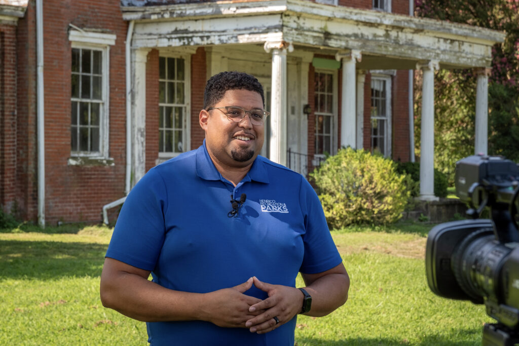 A man smiles standing in front of a historic home.