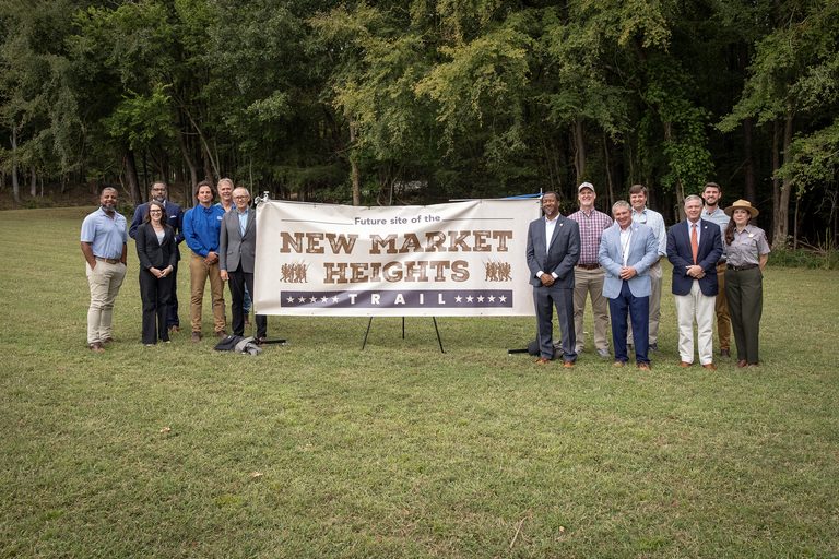 Henrico County officials and partners pose with a banner that says "future site of the New Market Heights Trail."