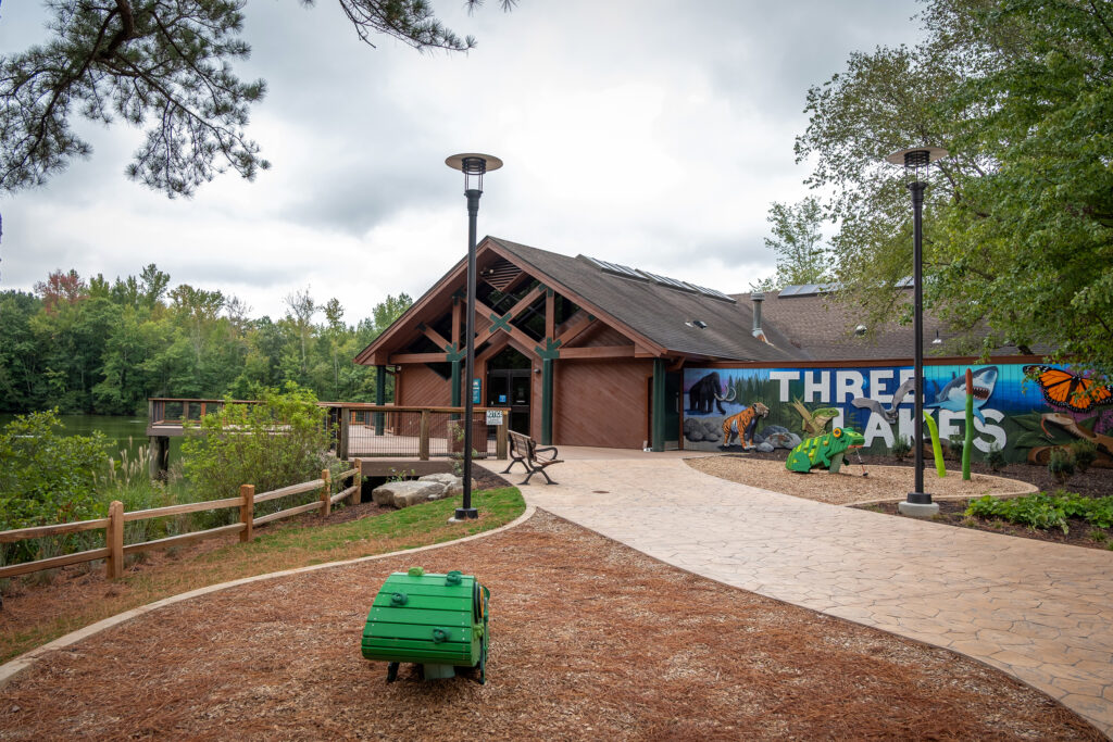 A photo shows a brown building at a park with walkways and a deck over a lake.