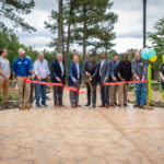 10 adults stand in a row to cut a red ribbon.