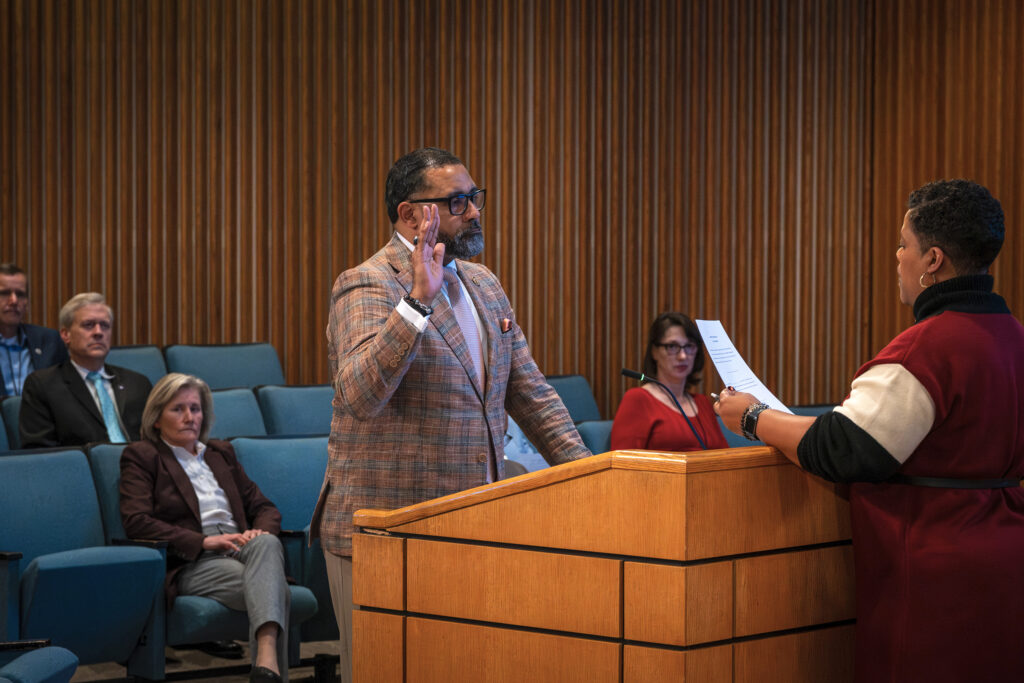 A photo of Supervisor Roscoe Cooper III, who is raising his right hand while being sworn in by a clerk as chair of the Board of Supervisors.