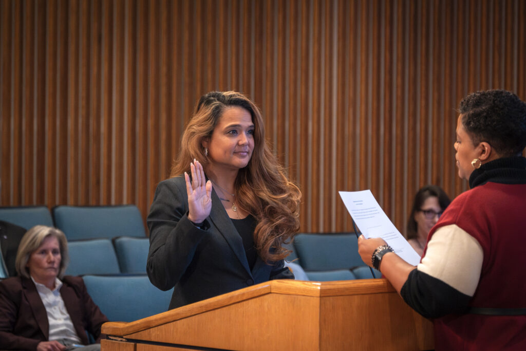 A woman stands at a podium with her hand raised to take an oath.