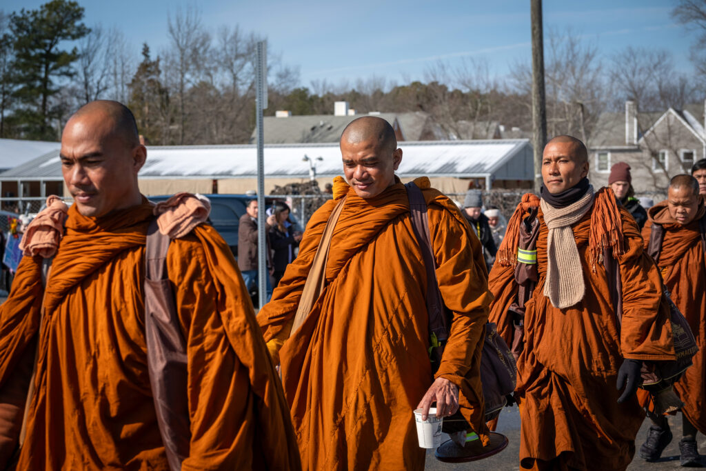 A monk wears orange robes and carries a cup of tea.