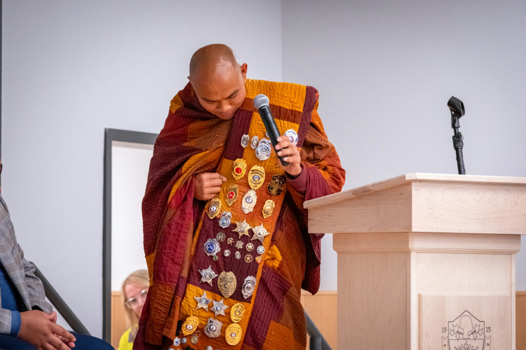 A monk shows a wide sash filled with gifted pins.