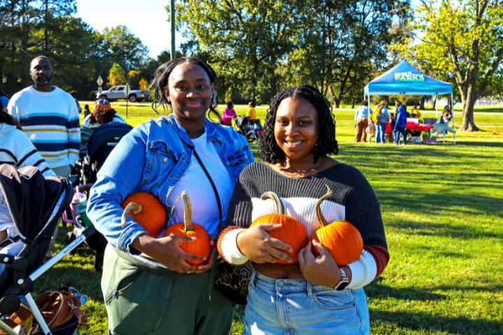 Two women holding pumpkins at fall event.