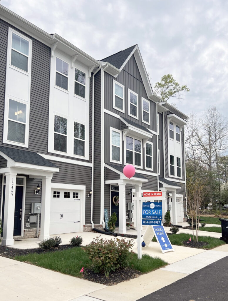 A row of grey and white townhomes with a for sale sign out front.
